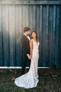 a bride and groom standing in front of a wooden fence