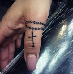 a person's hand with a cross tattoo on the middle finger and a chain around it