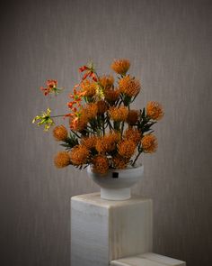 an arrangement of flowers in a white vase on top of a block of concrete against a gray wall