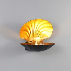 a golden shell shaped light fixture on a gray wall with a black bowl underneath it