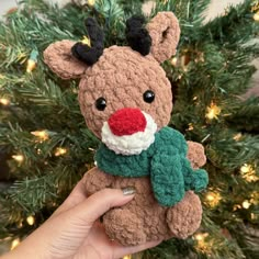 a hand holding a small stuffed animal in front of a christmas tree