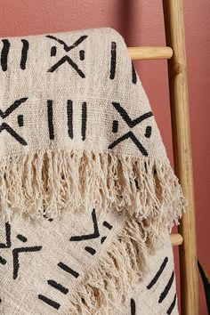 a blanket with black and white designs on it hanging from a wooden chair against a pink wall