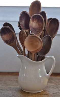 a white pitcher filled with wooden spoons on top of a table