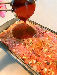 someone pouring sauce on top of a pizza in a pan