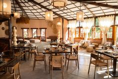 the inside of a restaurant with tables, chairs and lamps hanging from the ceiling in front of windows