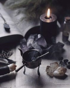 an open book sitting on top of a table next to a candle and some rocks