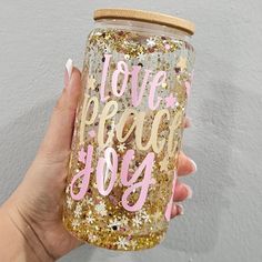 a hand holding a glittered mason jar with the words love, peace and joy on it