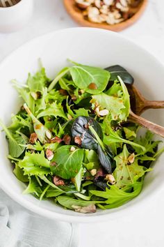 a white bowl filled with greens and nuts