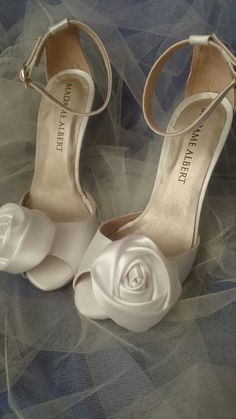 two white shoes with flowers on them sitting on top of a blue cloth covered floor