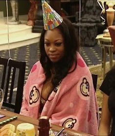 a woman sitting at a table wearing a pink robe and a party hat on her head