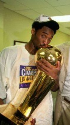 two men are holding trophies and posing for the camera in an office setting, one is wearing a white t - shirt