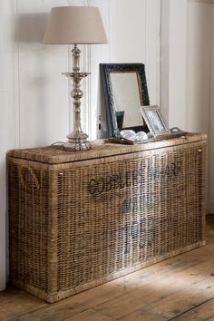 a wicker chest with a lamp on top and pictures in the basket underneath it