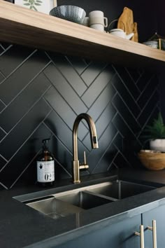 a kitchen with black tiles and gold faucet in the sink, next to a wooden shelf