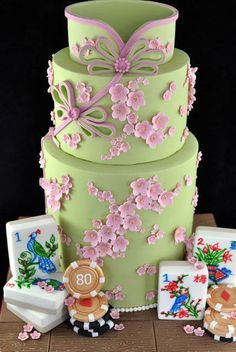 a three tiered green cake with pink flowers and decorations on the top, sitting on a wooden table