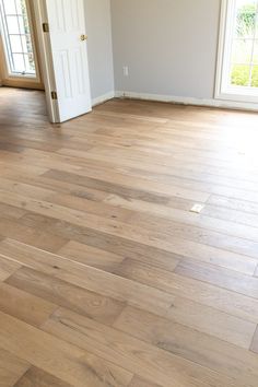 an empty living room with hard wood flooring and white door leading to another room