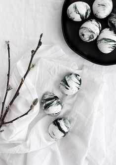 marbles are sitting on a white cloth next to a black plate and twig