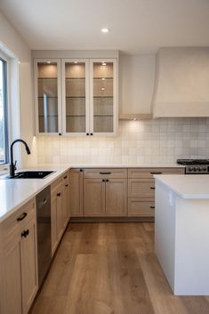 an empty kitchen with wooden floors and white counter tops, along with lots of cupboards