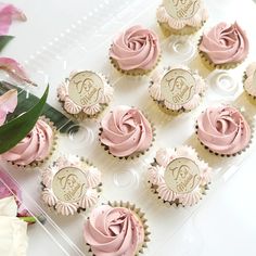 cupcakes with pink frosting and monogrammed icing are arranged on a clear tray