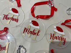 christmas ornament ornaments with name and santa hat hanging from red ribbon on white table