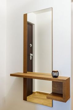 a wooden shelf with a mirror and vase sitting on it's side in front of a white wall