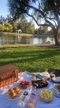 a picnic table with bread, fruit and water on it in front of a lake