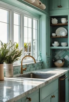 a kitchen with green cabinets, marble counter tops and gold faucet pulls on the cabinet doors