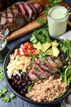 a bowl filled with meat, rice and veggies next to a glass of ranch dressing