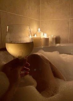 a glass of wine sitting in the middle of a bathtub filled with bubbles and candles