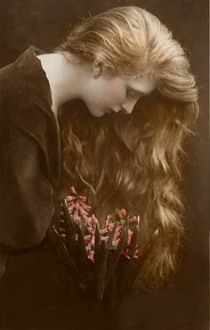 a woman with long hair holding a bunch of flowers in her hand and looking down at the ground