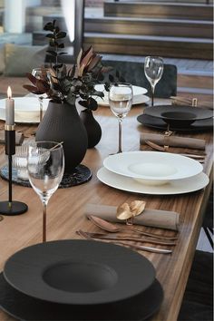 the table is set with black and white plates, silverware, and wine glasses