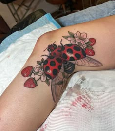 a ladybug tattoo on the leg of a woman with strawberrys and daisies