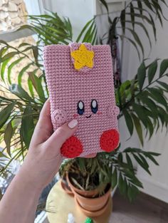 a hand holding up a pink case with a smiley face on it, in front of a potted plant