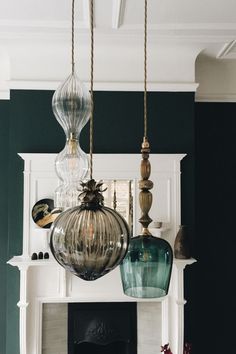 three glass pendants hanging from the ceiling above a fireplace in a living room with green walls