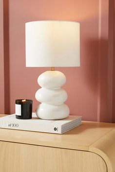 a white lamp sitting on top of a wooden table next to a book and cup