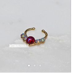 a gold nose ring with red and blue stones on the outside, sitting in snow