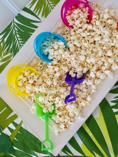 three plastic spoons are sitting on a plate with popcorn and other items in it