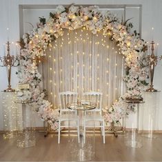 a table with white chairs and flowers on it in front of a curtained backdrop