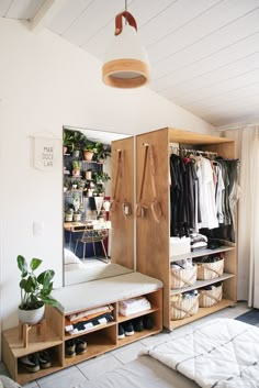 a bedroom with a bed, mirror and closet full of clothes on shelves next to a potted plant