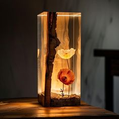 a glass vase with a flower in it on top of a wooden table next to a wall