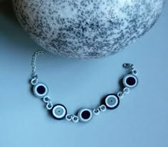 a close up of a bracelet on a table next to a bowl with a fruit