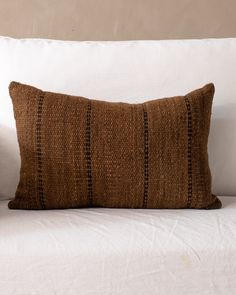 a brown and black striped pillow sitting on top of a white couch next to a wall