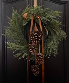 a wreath with pine cones and ribbons hanging from it's side on a door