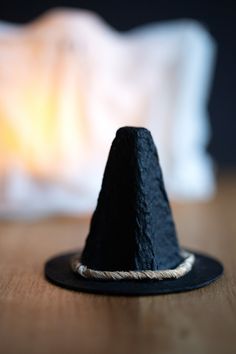 a small black hat sitting on top of a wooden table next to a white pillow