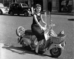 a woman riding on the back of a scooter with a basket strapped to it