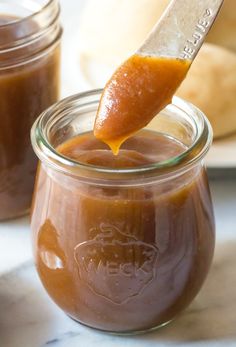 a spoon full of caramel sauce on top of a jar with another jar in the background