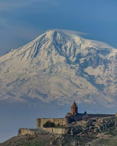 an old castle on top of a hill with a large snow covered mountain in the background