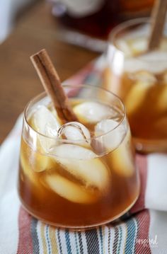 two glasses filled with ice and cinnamon on top of a table next to a napkin