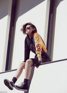 a woman sitting on the edge of a wall with her legs crossed and wearing sunglasses