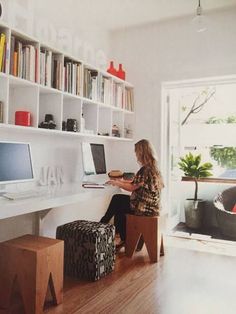 a woman sitting in front of a computer on top of a white desk next to a window