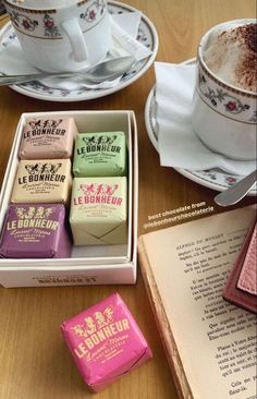 four different types of chocolates in a box on a table next to an open book